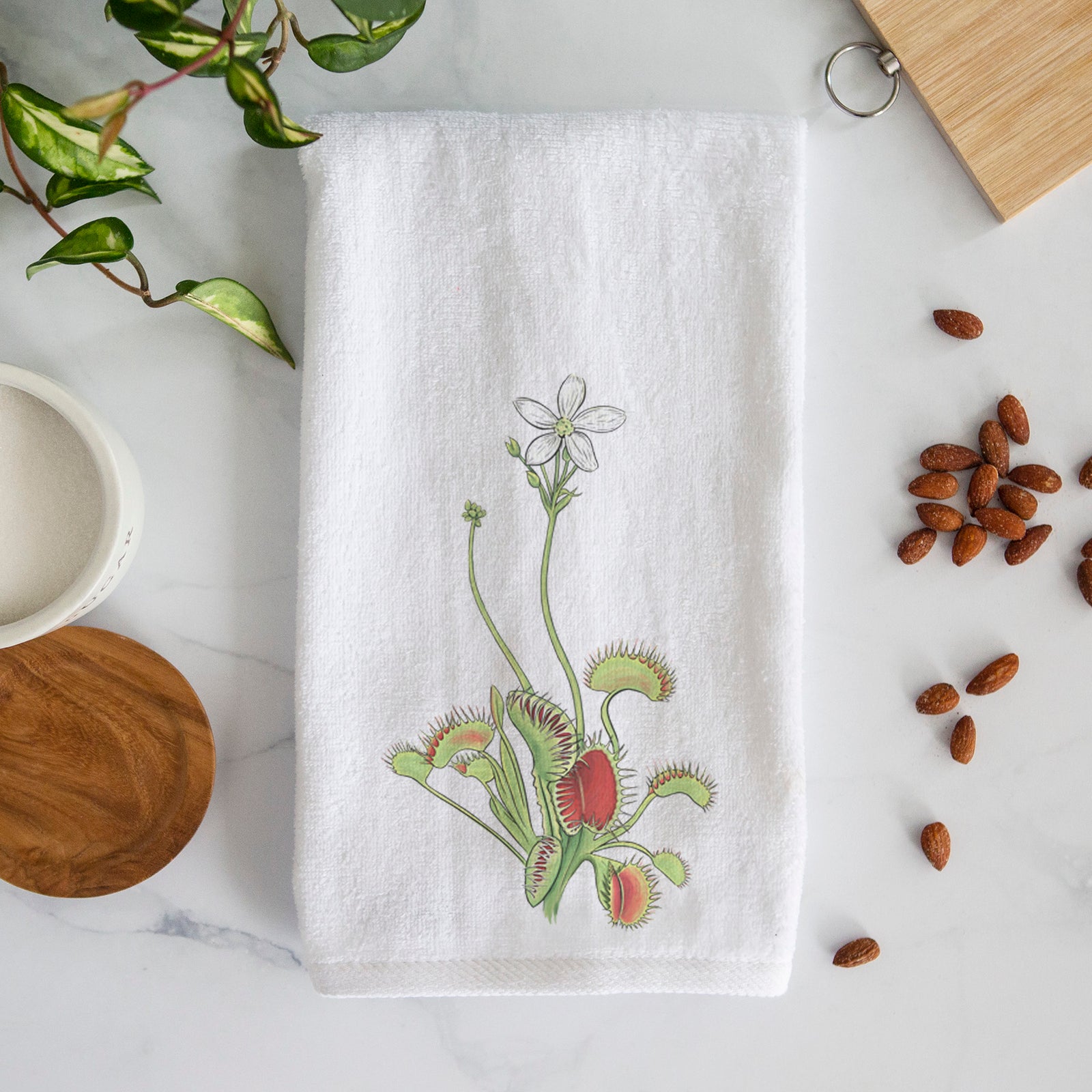 White hand towel printed with a full-color illustration of a Venus flytrap plant with red traps and a small white flower.