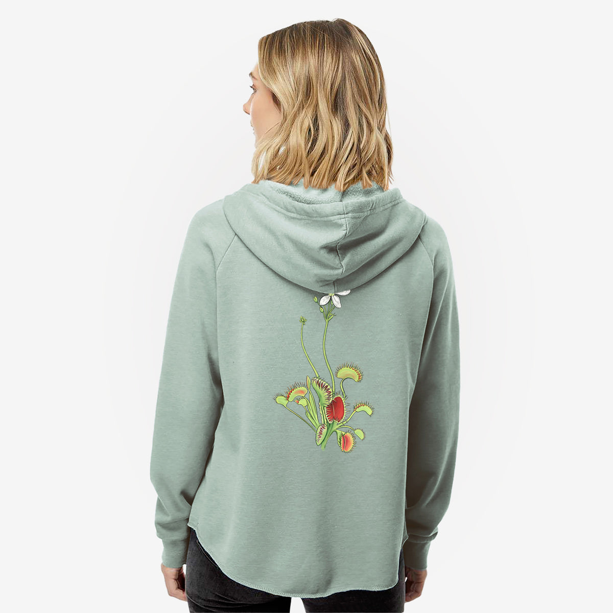 Woman wearing a sage green women's Cali Wave zip-up sweatshirt printed with a full-color illustration of a Venus flytrap plant with red traps and a small white flower, seen from behind.