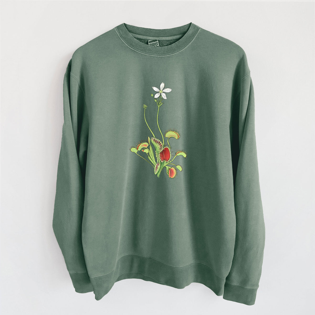 Alpine green pigment dyed crewneck sweatshirt laid flat, printed with a full-color illustration of a Venus flytrap plant with red traps and a small white flower.