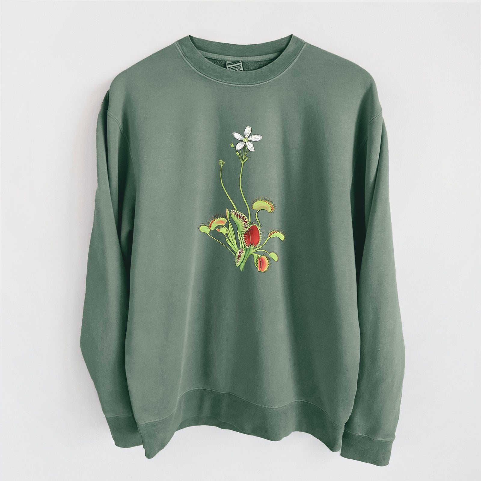 Alpine green pigment dyed crewneck sweatshirt laid flat, printed with a full-color illustration of a Venus flytrap plant with red traps and a small white flower.
