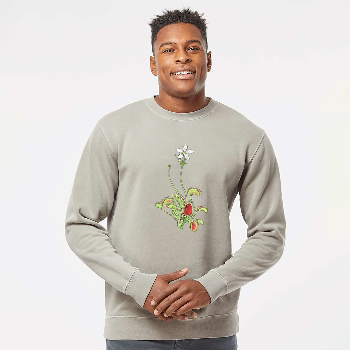 Model wearing a cement grey pigment dyed crewneck sweatshirt printed with a full-color illustration of a Venus flytrap plant with red traps and a small white flower.
