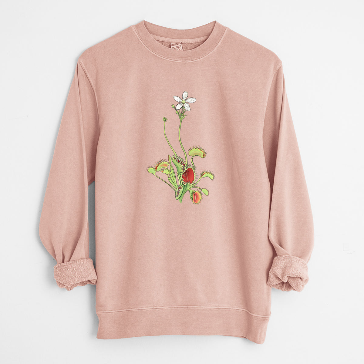 Dusty pink pigment dyed crewneck sweatshirt laid flat with the sleeves rolled, printed with a full-color illustration of a Venus flytrap plant with red traps and a small white flower.
