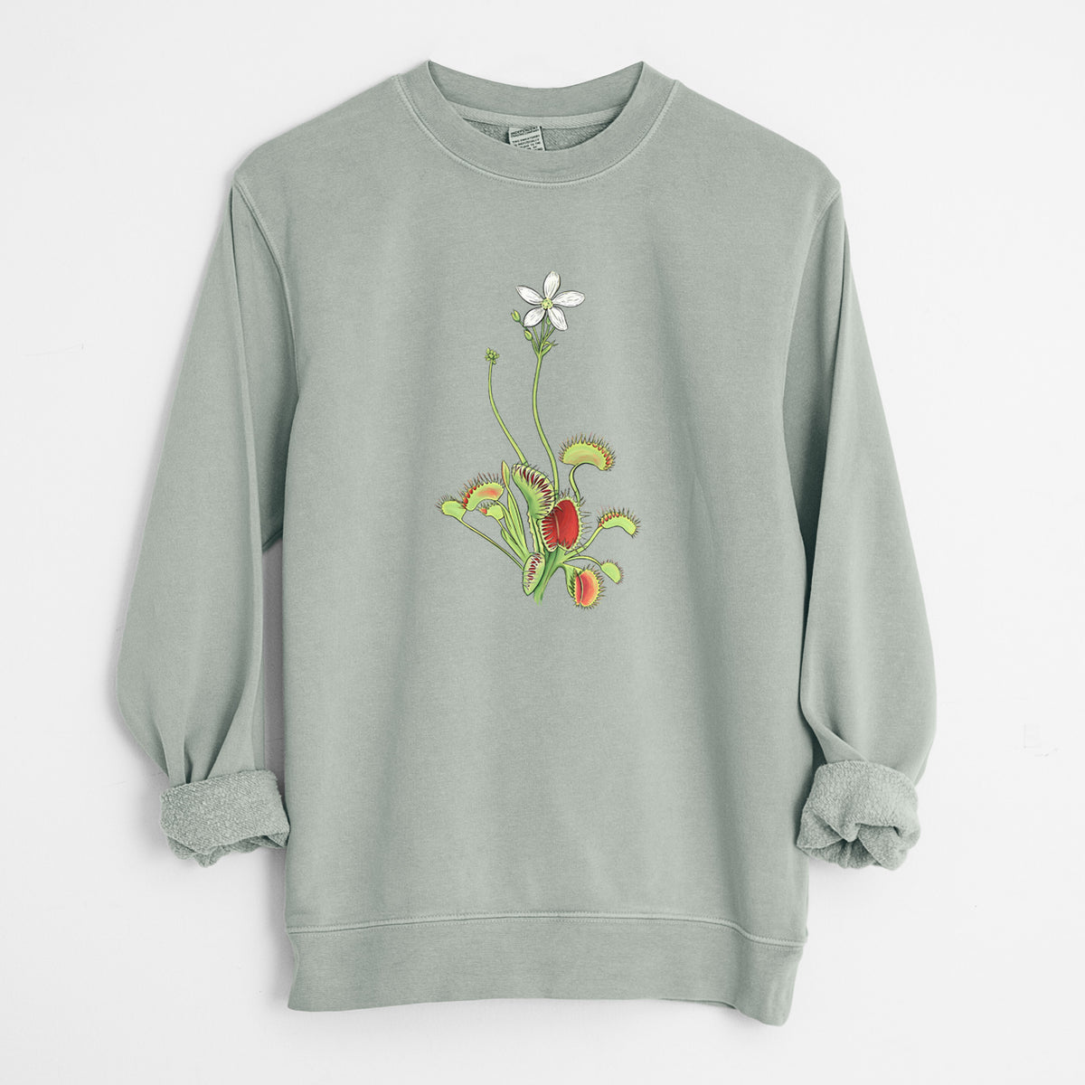 Sage green pigment dyed crewneck sweatshirt laid flat with the sleeves rolled, printed with a full-color illustration of a Venus flytrap plant with red traps and a small white flower.