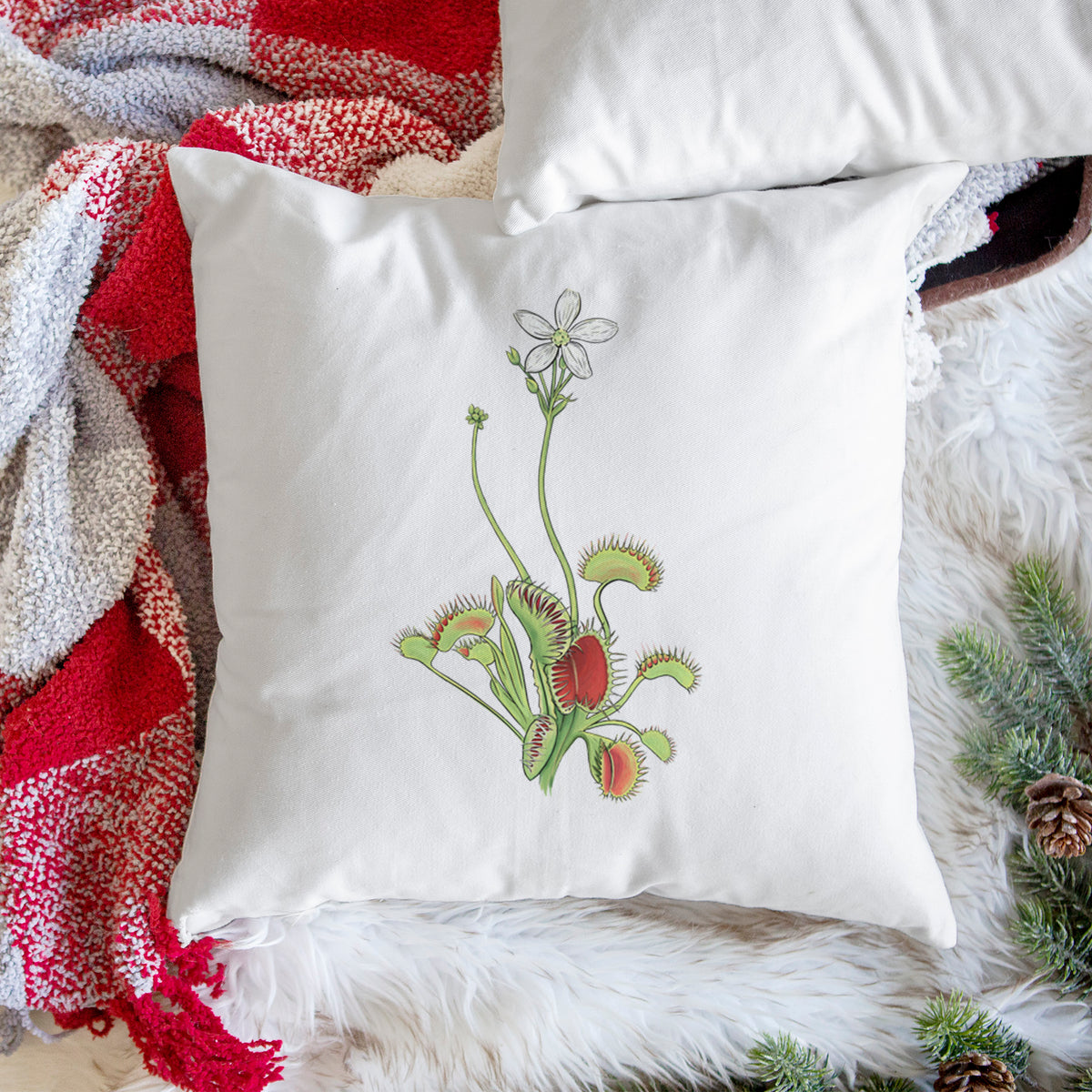 White pillow cover printed with a full-color illustration of a Venus flytrap plant with red traps and a small white flower, on a woven chair.