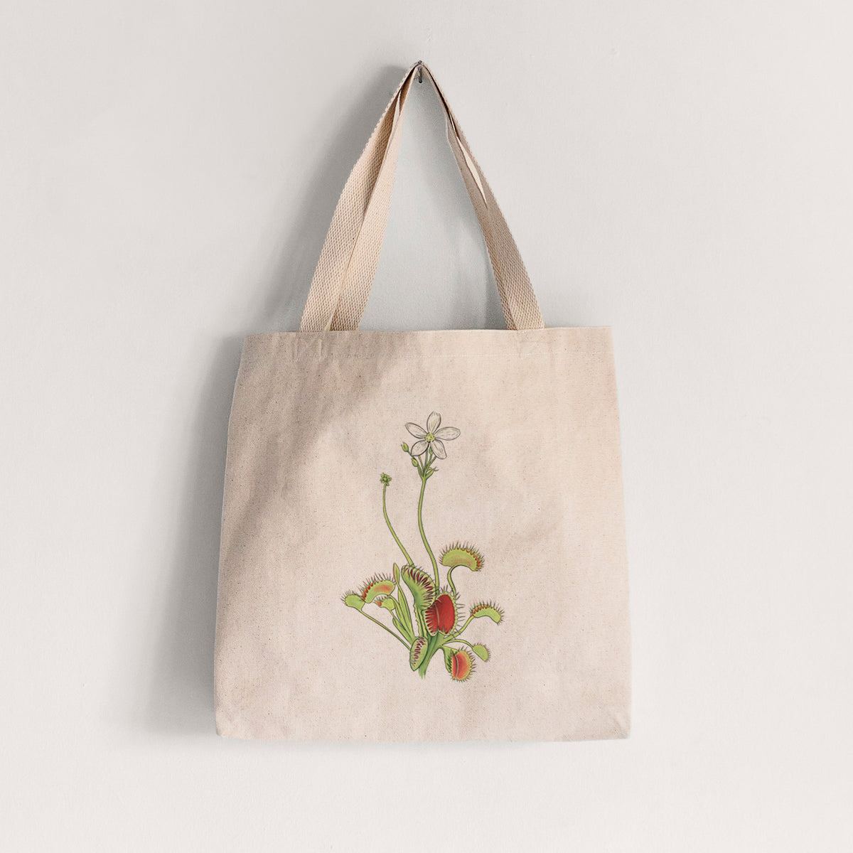 Natural canvas tote bag printed with a full-color illustration of a Venus flytrap plant with red traps and a small white flower.