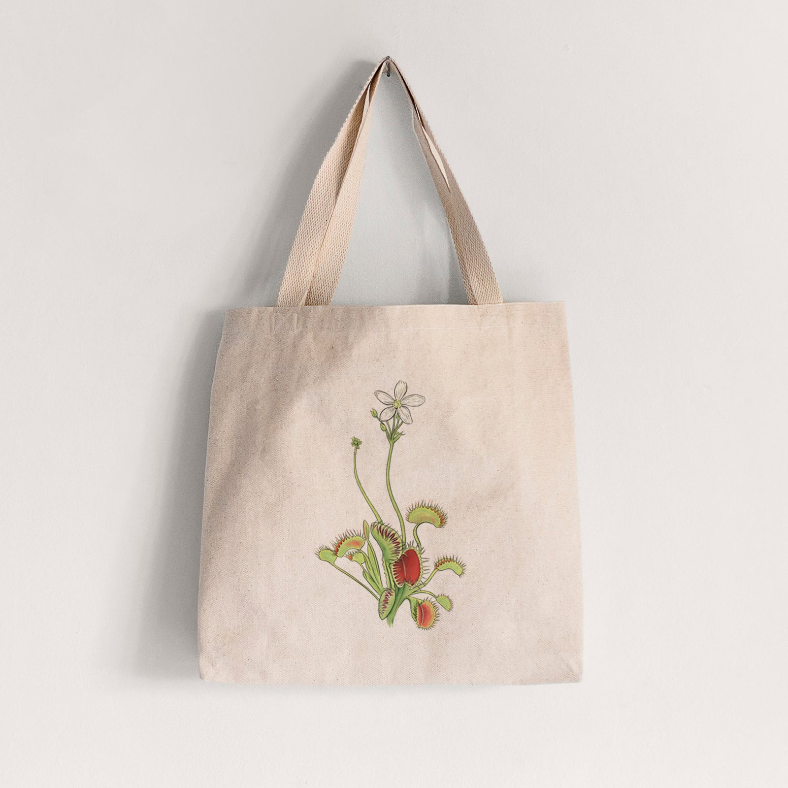 Natural canvas tote bag printed with a full-color illustration of a Venus flytrap plant with red traps and a small white flower.