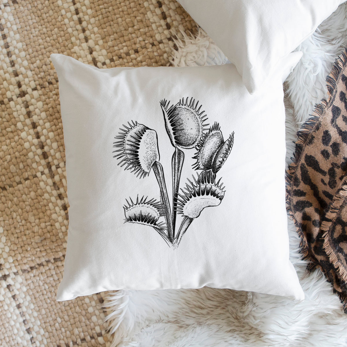 White pillow cover printed with a black ink illustration of a Venus flytrap plant with open traps, on a woven chair.