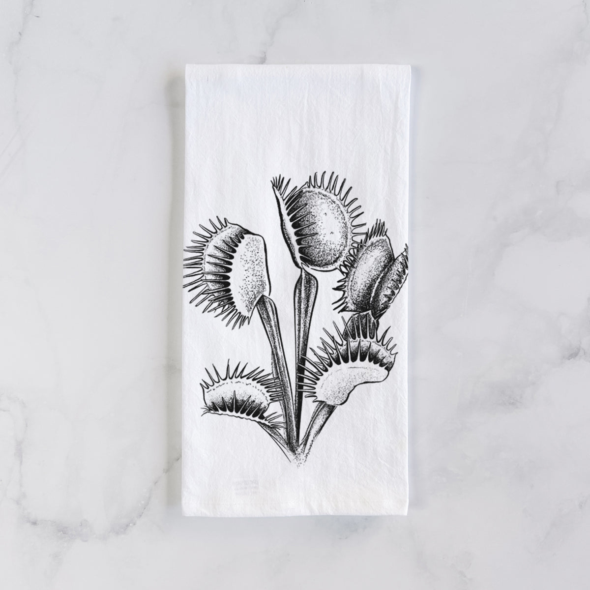 White cotton tea towel laid flat on marble, printed with a black ink illustration of a Venus flytrap plant with open traps.