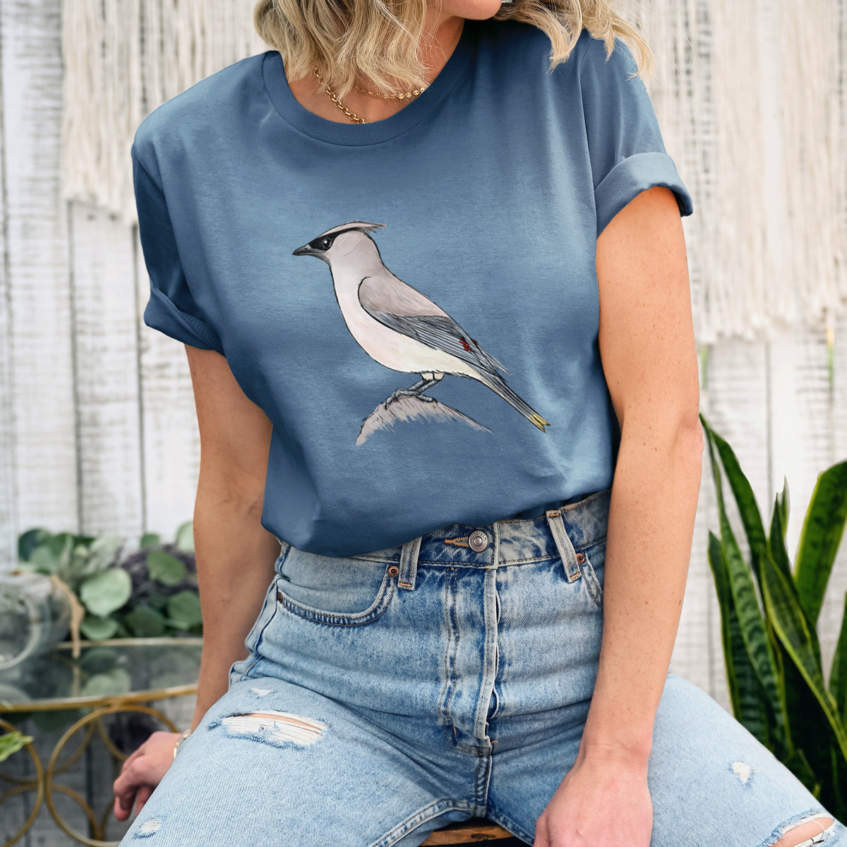 Woman wearing a steel blue lightweight cotton t-shirt printed with a full-color illustration of a cedar waxwing perched on a branch.