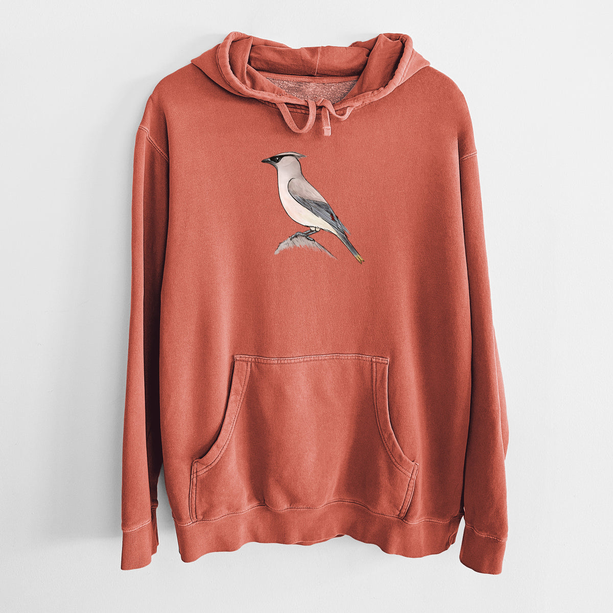 Amber orange pigment dyed hoodie laid flat, printed with a full-color illustration of a cedar waxwing perched on a branch.