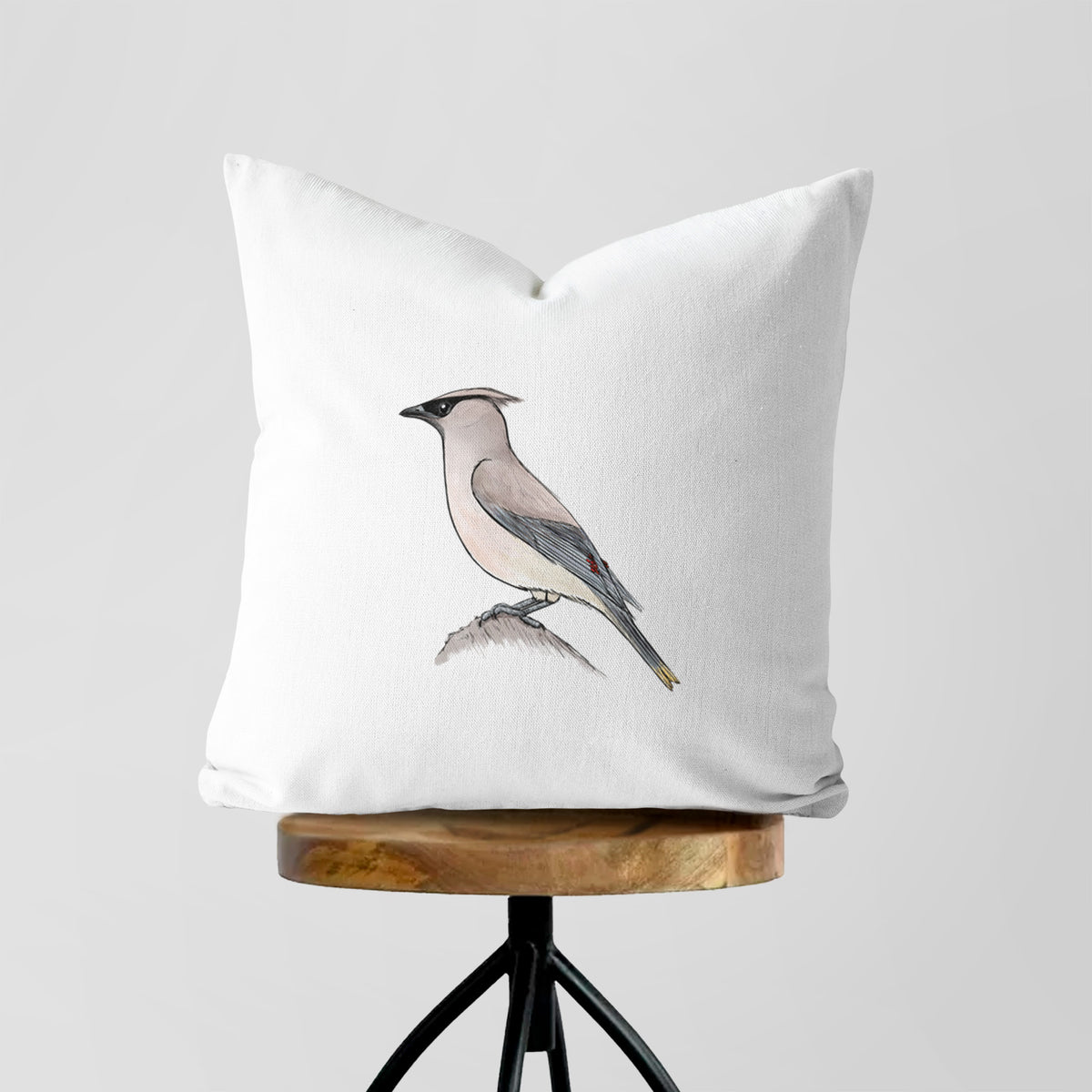 White pillow cover printed with a full-color illustration of a cedar waxwing perched on a branch, on a wooden stool.