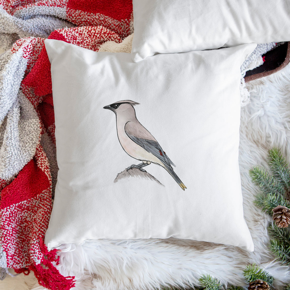 White pillow cover printed with a full-color illustration of a cedar waxwing perched on a branch, on a woven chair.