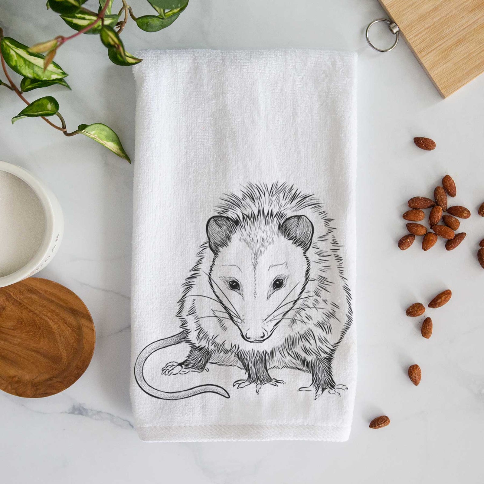White hand towel printed with a detailed black ink illustration of a Virginia opossum standing with its long tail curled.