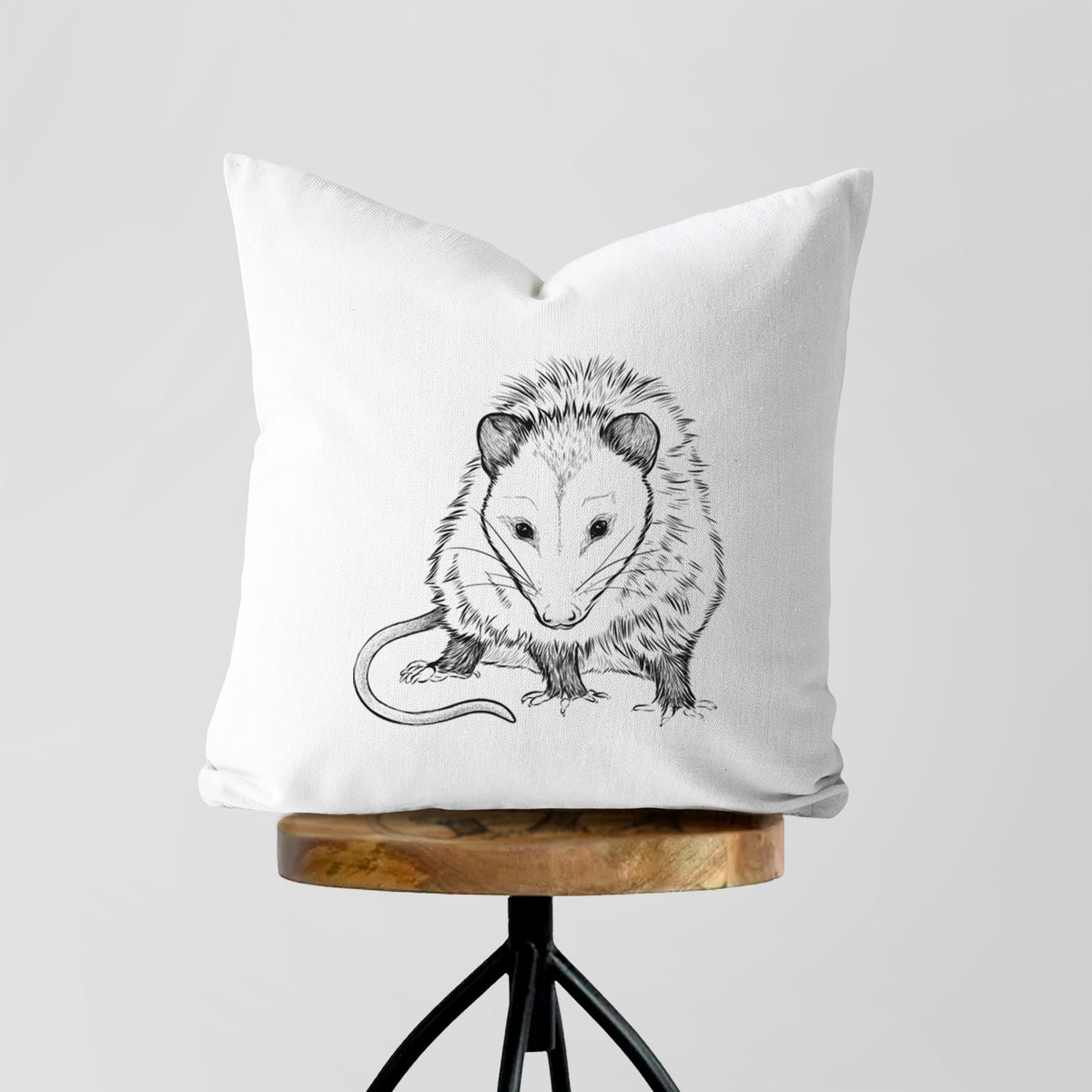 White pillow cover printed with a detailed black ink illustration of a Virginia opossum standing with its long tail curled, on a wooden stool.