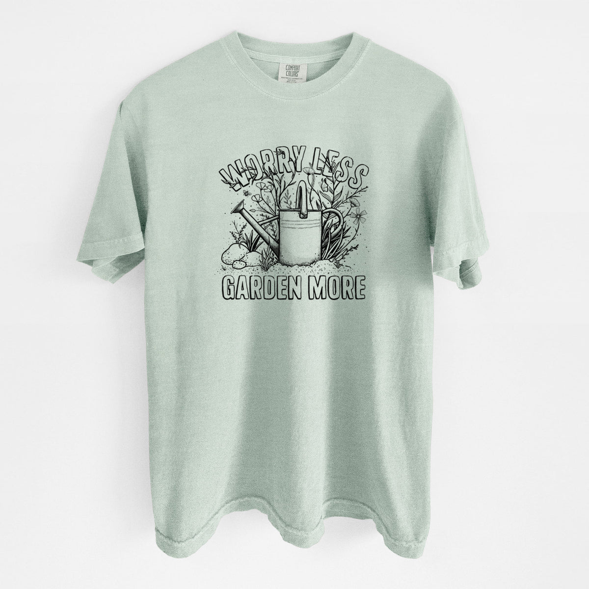 Bay green Comfort Colors t-shirt laid flat, printed with a black ink watering can surrounded by flowers and garden tools, with the words Worry Less, Garden More.