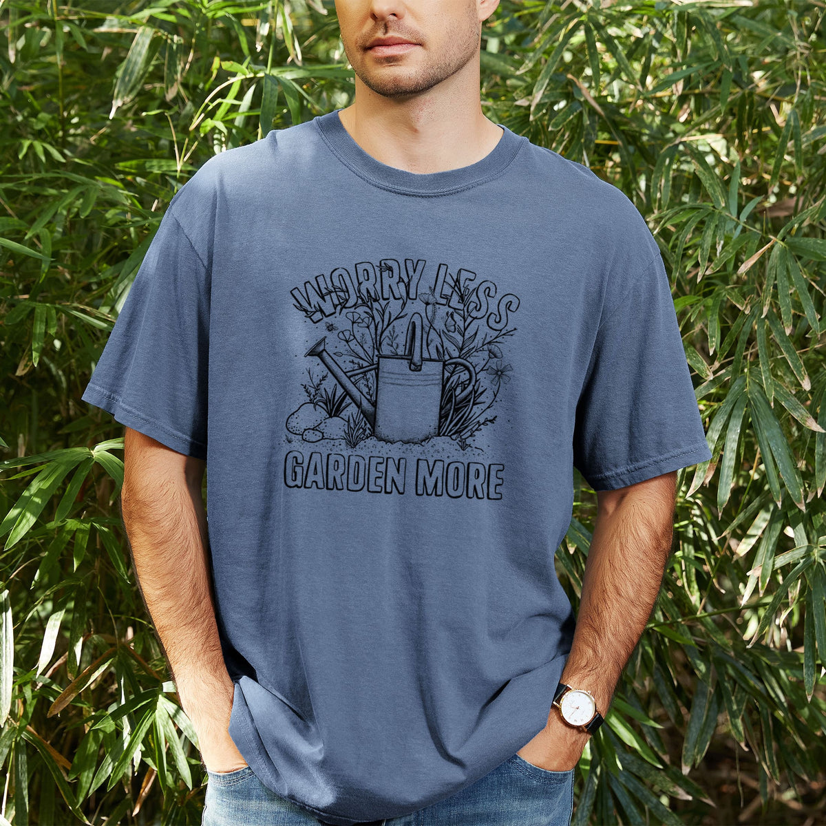 Man wearing a Comfort Colors t-shirt printed with a black ink watering can surrounded by flowers and garden tools, with the words Worry Less, Garden More, outdoors.