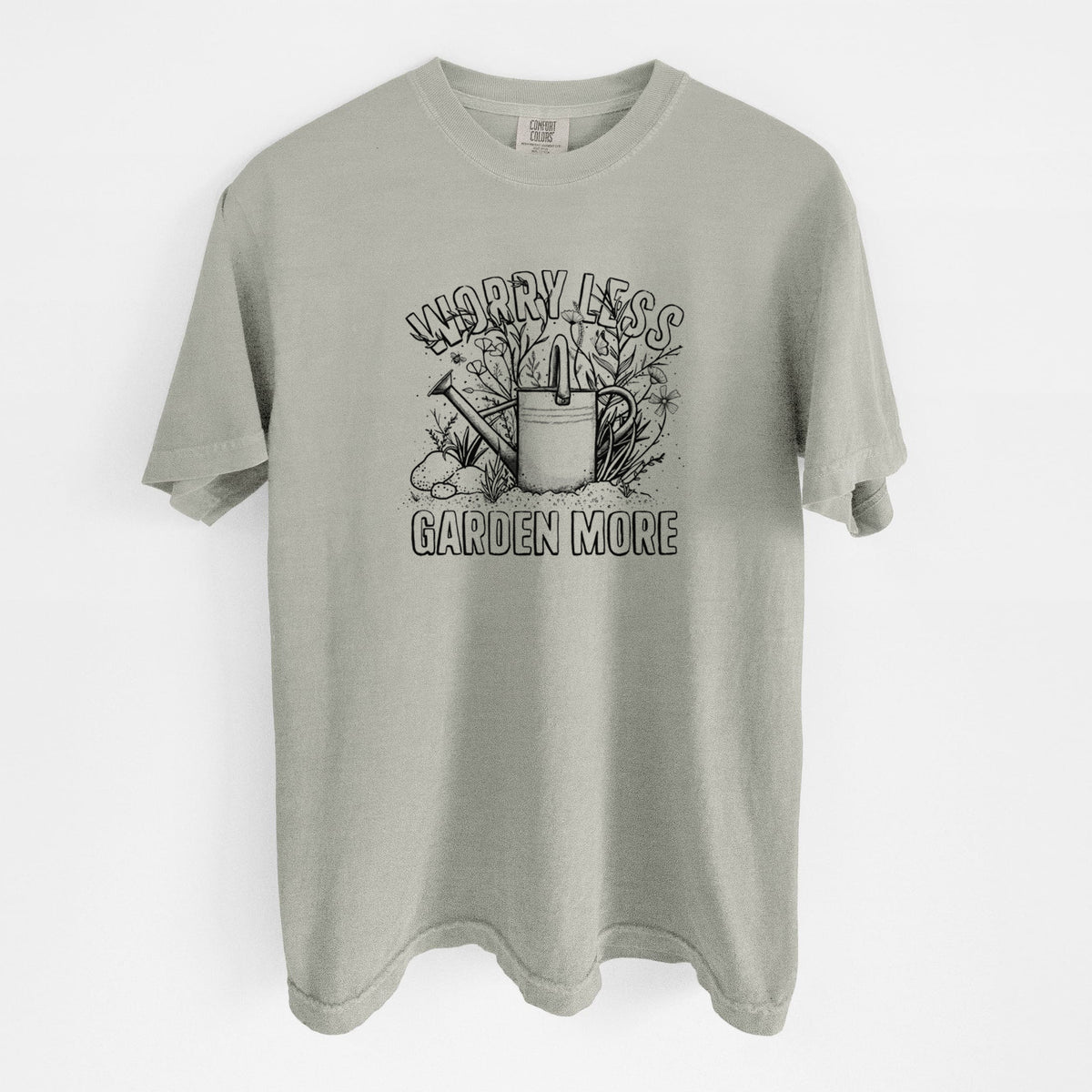 Sandstone beige Comfort Colors t-shirt laid flat, printed with a black ink watering can surrounded by flowers and garden tools, with the words Worry Less, Garden More.