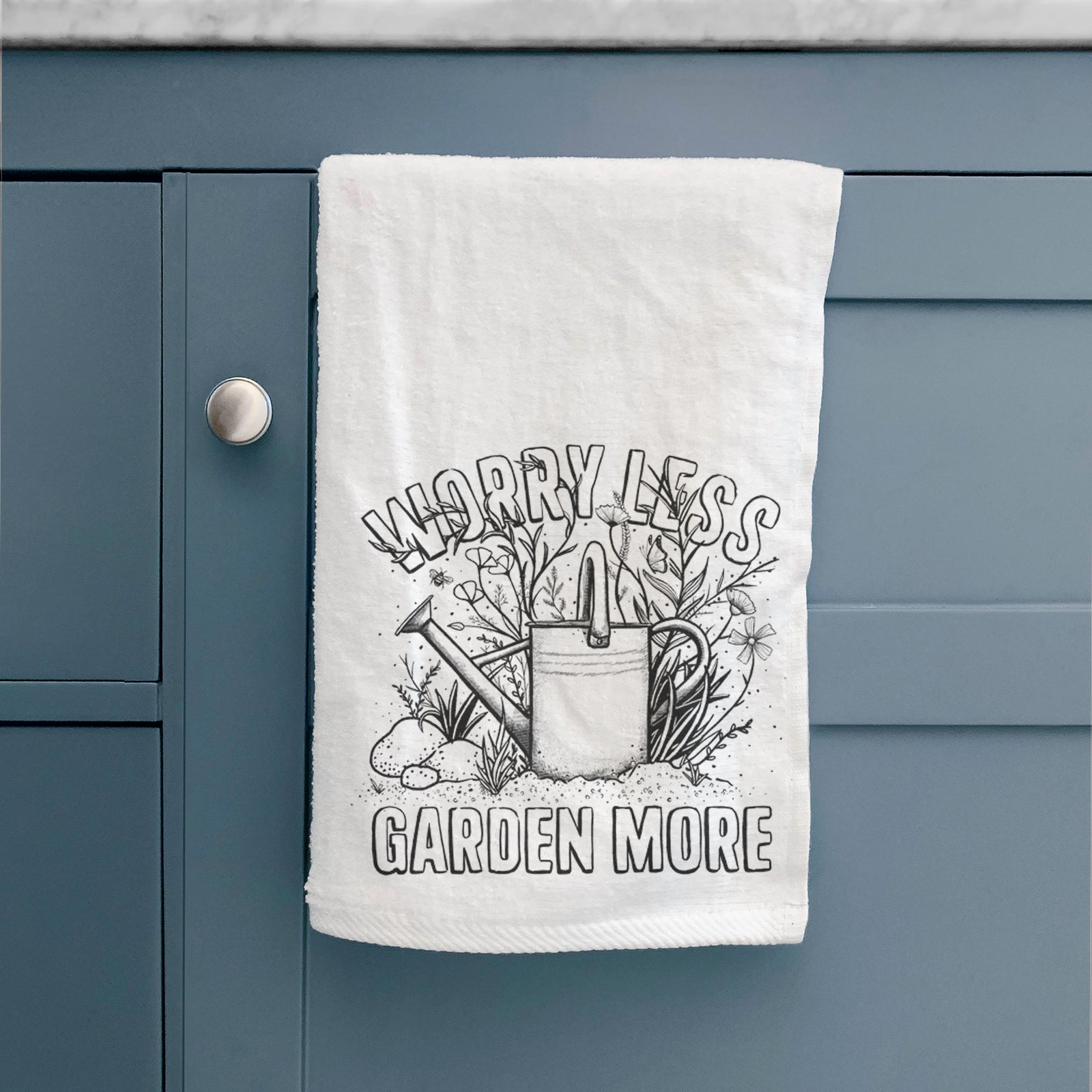 White hand towel printed with a black ink watering can surrounded by flowers and garden tools, with the words Worry Less, Garden More.