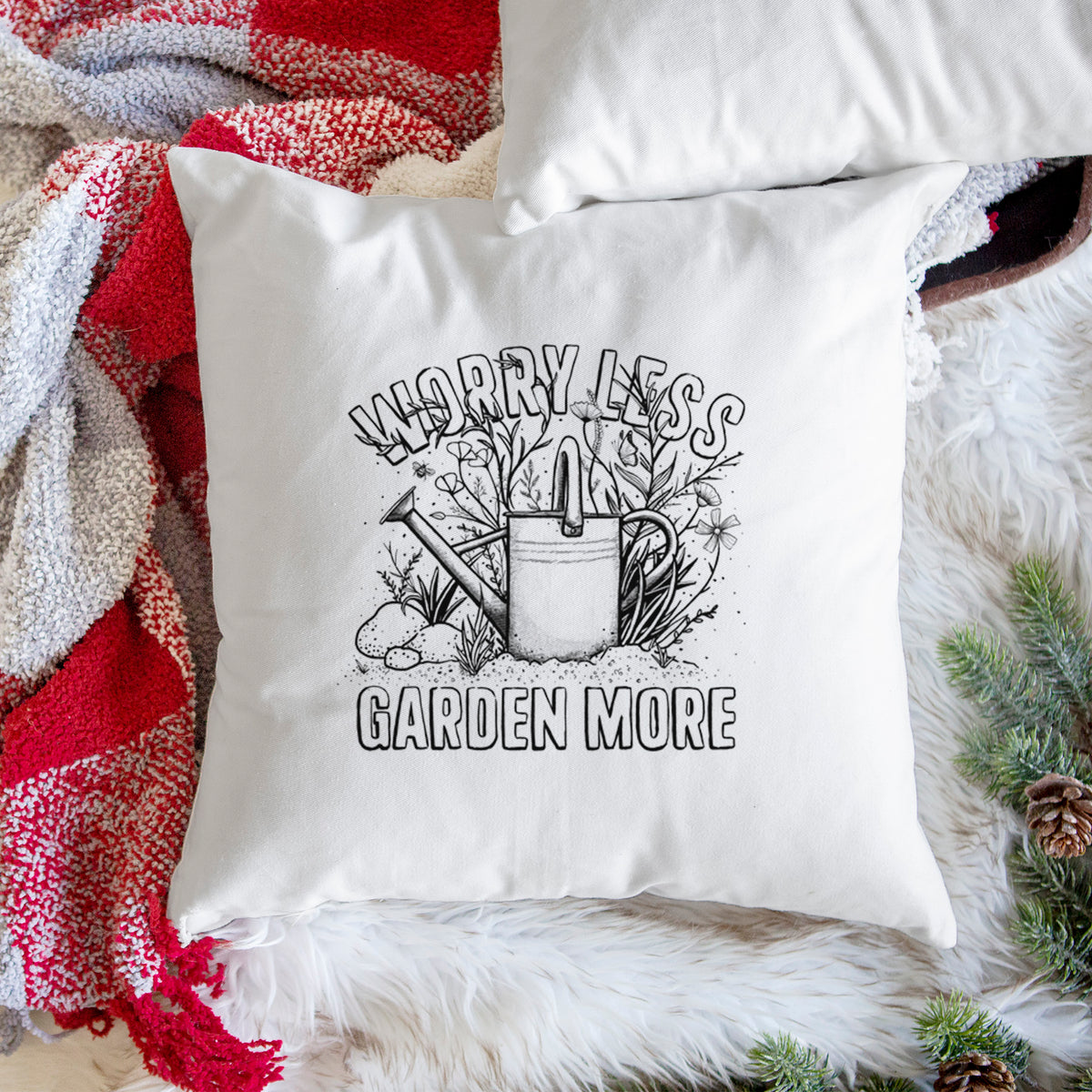 White pillow cover printed with a black ink watering can surrounded by flowers and garden tools, with the words Worry Less, Garden More, on a woven chair.