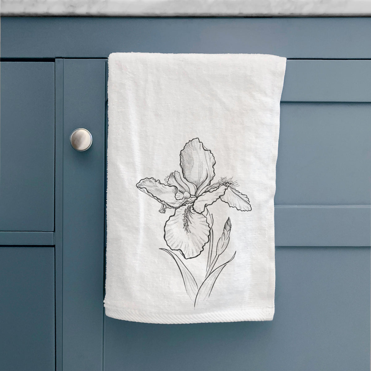 White hand towel printed with a black ink line drawing of a wall iris flower on its stem, hanging on a cabinet door.