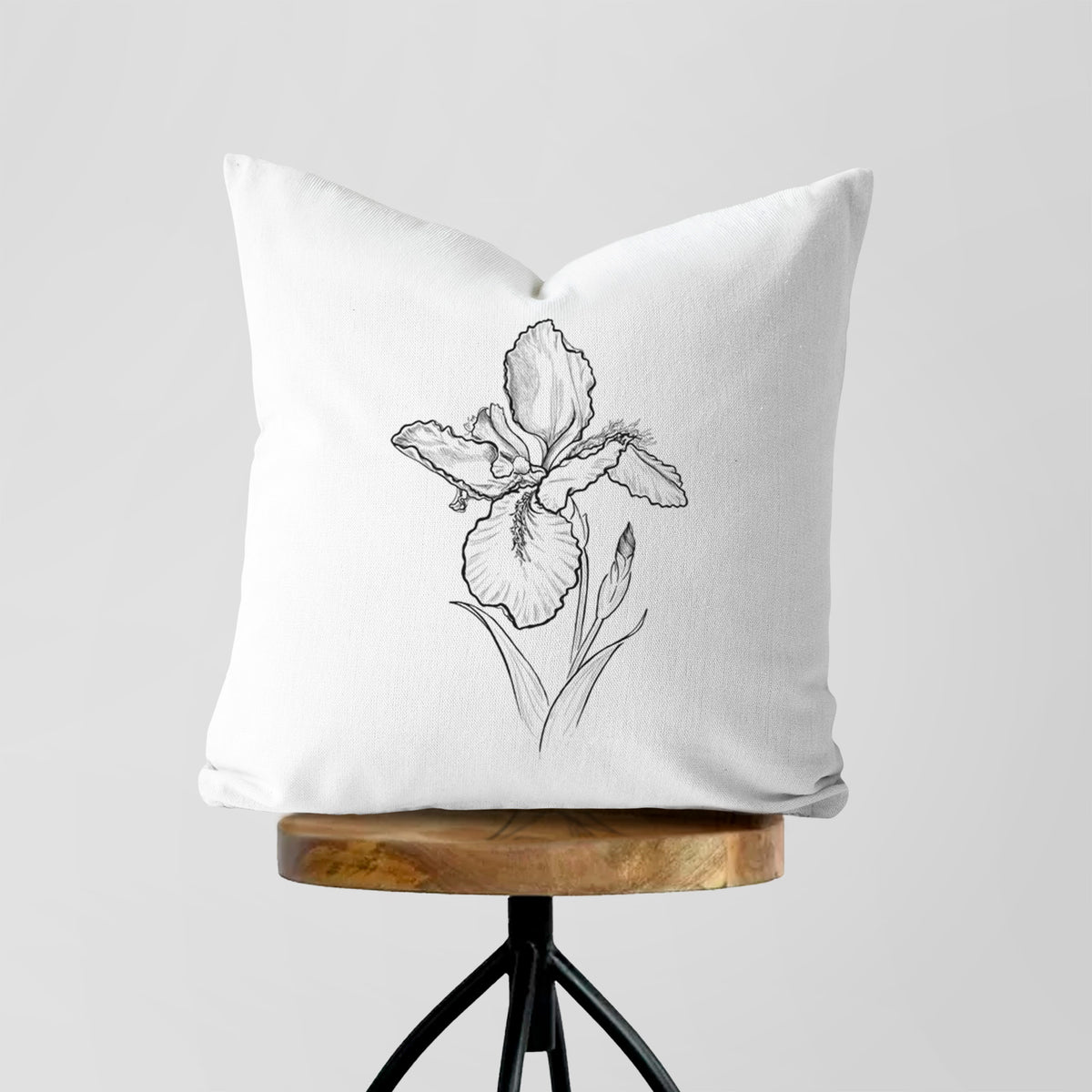 White pillow cover printed with a black ink line drawing of a wall iris flower on its stem, on a wooden stool.