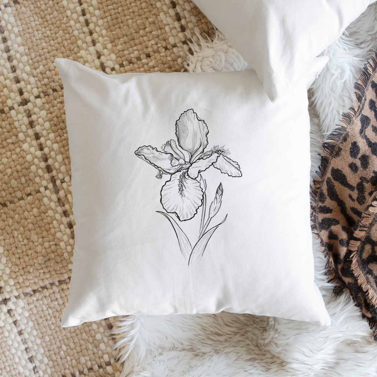 White pillow cover printed with a black ink line drawing of a wall iris flower on its stem, on a woven chair.