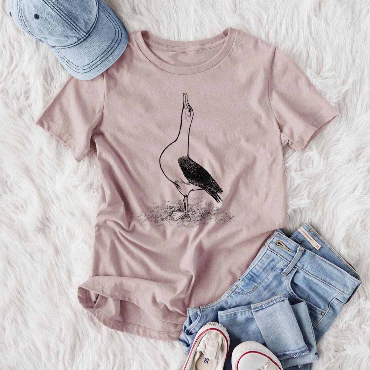 Women's relaxed fit cotton t-shirt printed with a black ink illustration of a wandering albatross with its head raised, styled flat on a white faux fur rug with jeans.
