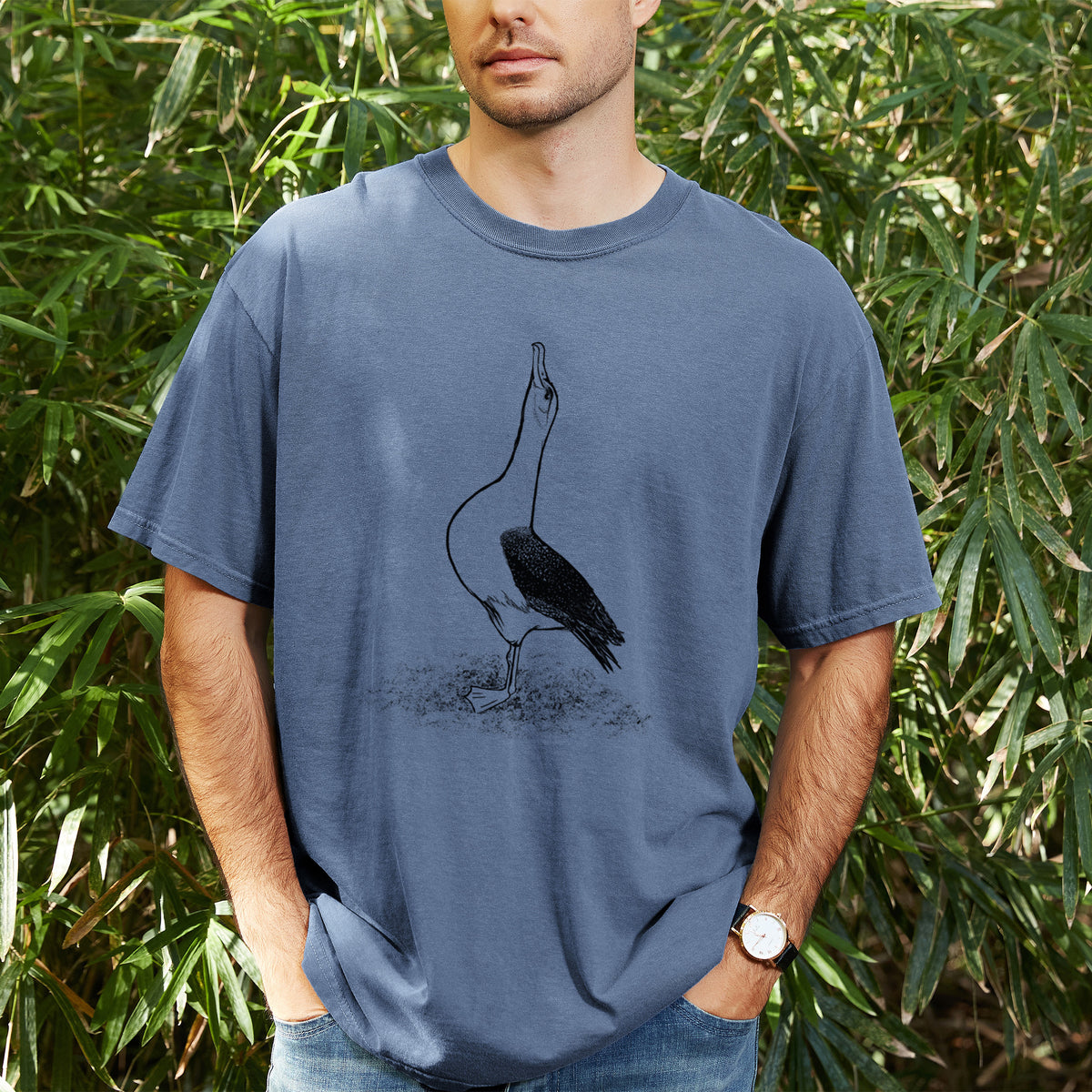 Man wearing a Comfort Colors t-shirt printed with a black ink illustration of a wandering albatross with its head raised, outdoors.