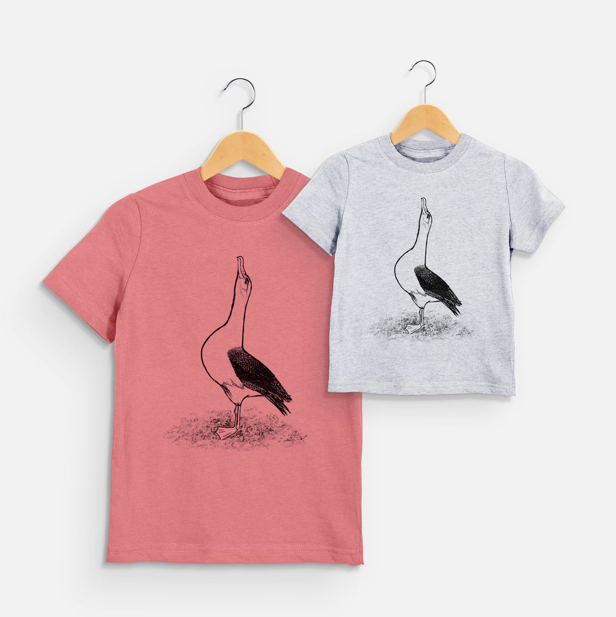 Two youth t-shirts in different colors on hangers, printed with a black ink illustration of a wandering albatross with its head raised.