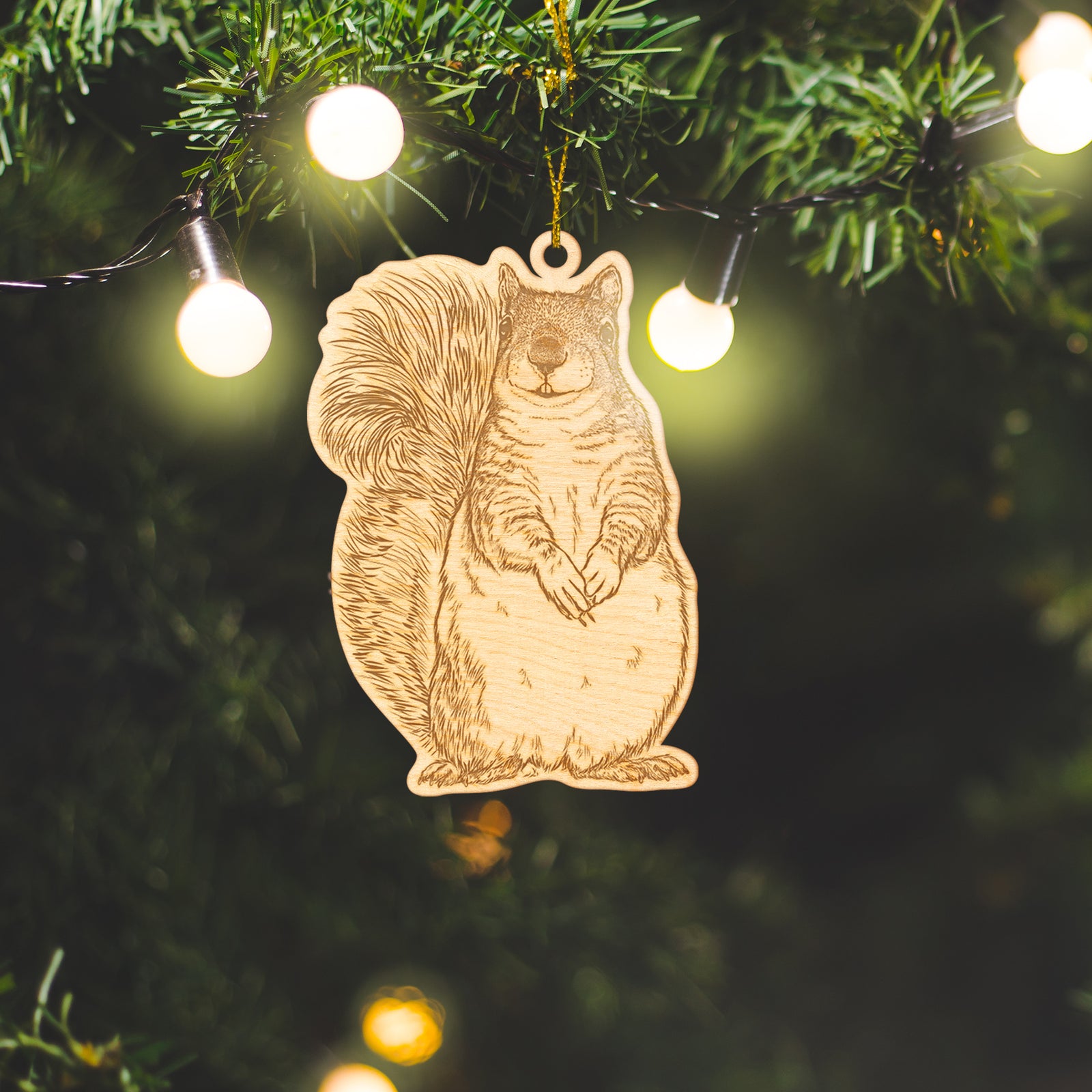 Wooden ornament featuring a detailed engraving of a western grey squirrel sitting upright with a bushy tail, on a knit blanket with pine cones.
