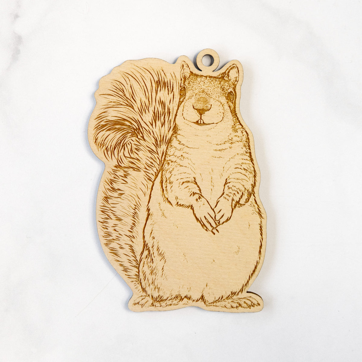 Wooden ornament featuring a detailed engraving of a western grey squirrel sitting upright with a bushy tail, on a marble surface.
