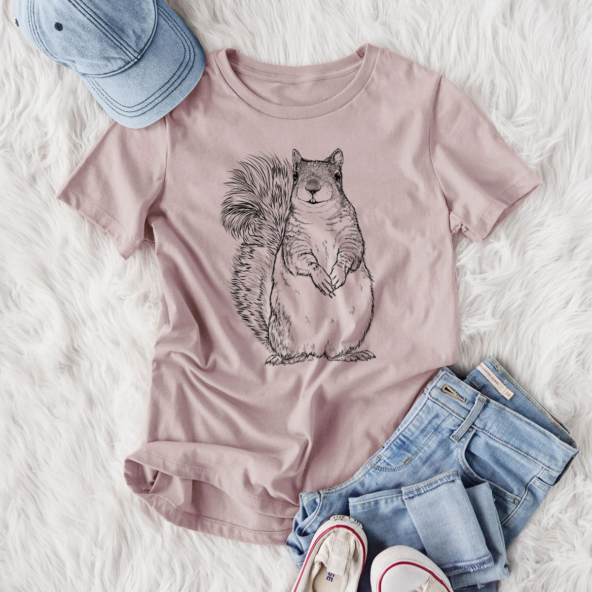 Women's relaxed fit cotton t-shirt printed with a detailed black ink illustration of a western grey squirrel sitting upright with a bushy tail, styled flat on a white faux fur rug with jeans.