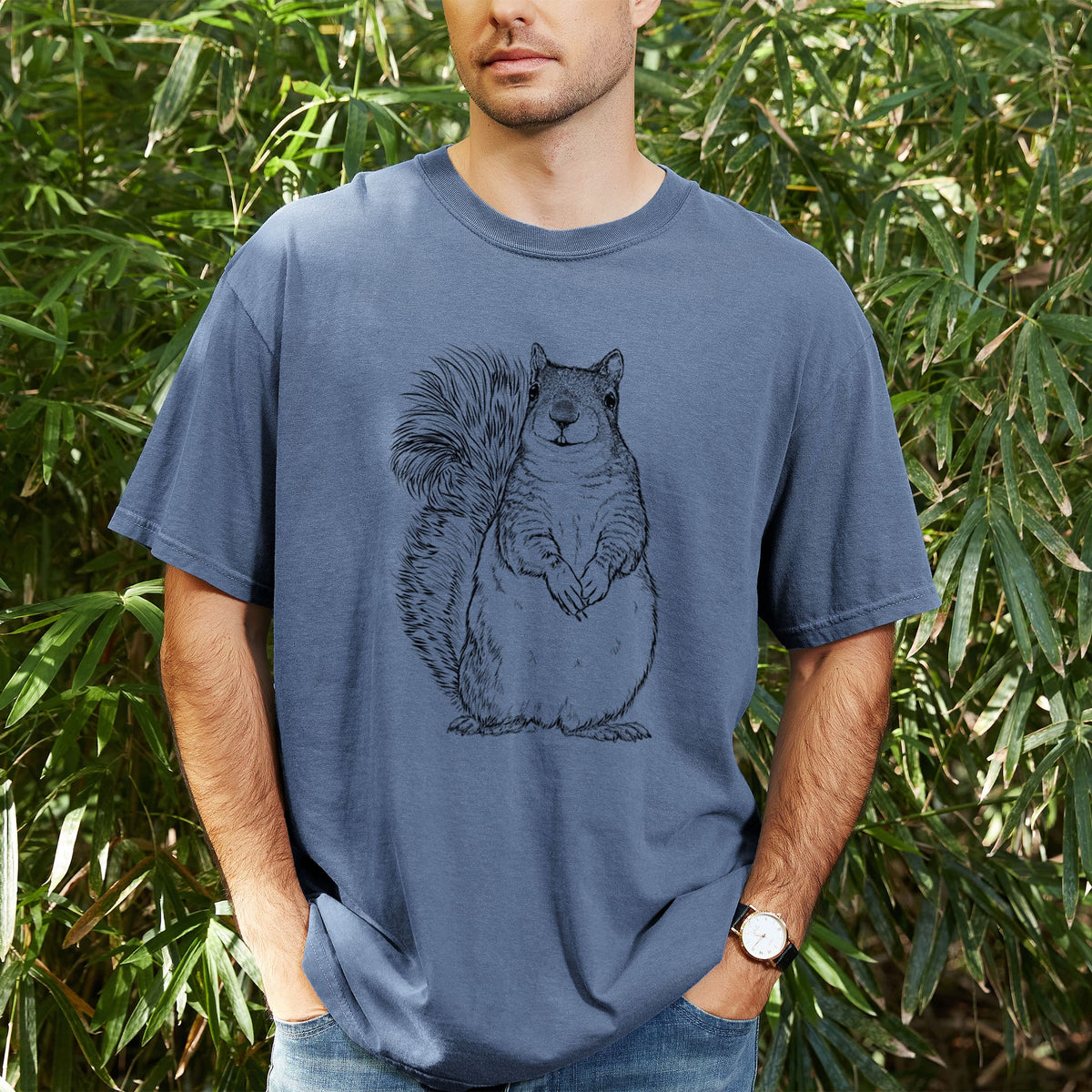 Man wearing a Comfort Colors t-shirt printed with a detailed black ink illustration of a western grey squirrel sitting upright with a bushy tail, outdoors.