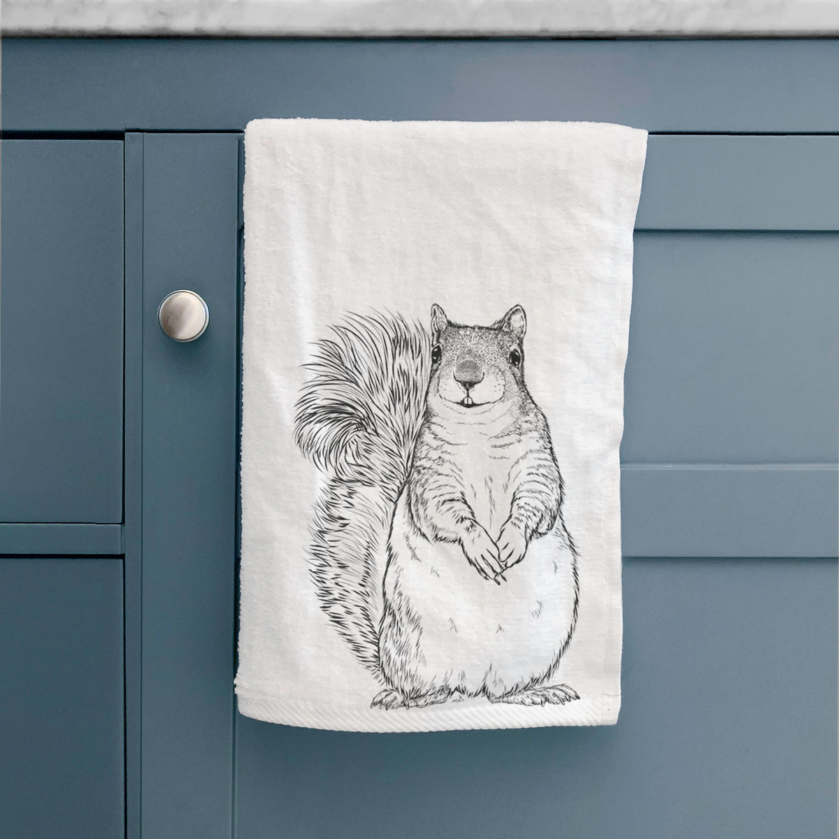 White hand towel printed with a detailed black ink illustration of a western grey squirrel sitting upright with a bushy tail, hanging on a cabinet door.