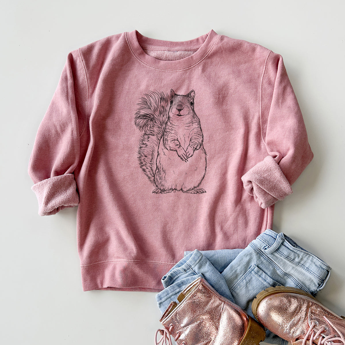 Youth crewneck sweatshirt printed with a detailed black ink illustration of a western grey squirrel sitting upright with a bushy tail, styled flat with jeans and boots.