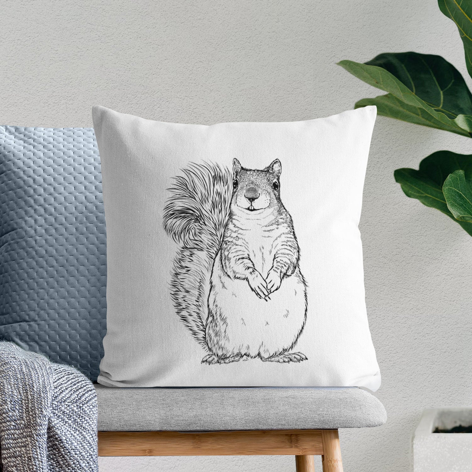 White pillow cover printed with a detailed black ink illustration of a western grey squirrel sitting upright with a bushy tail, on a bench beside plants.
