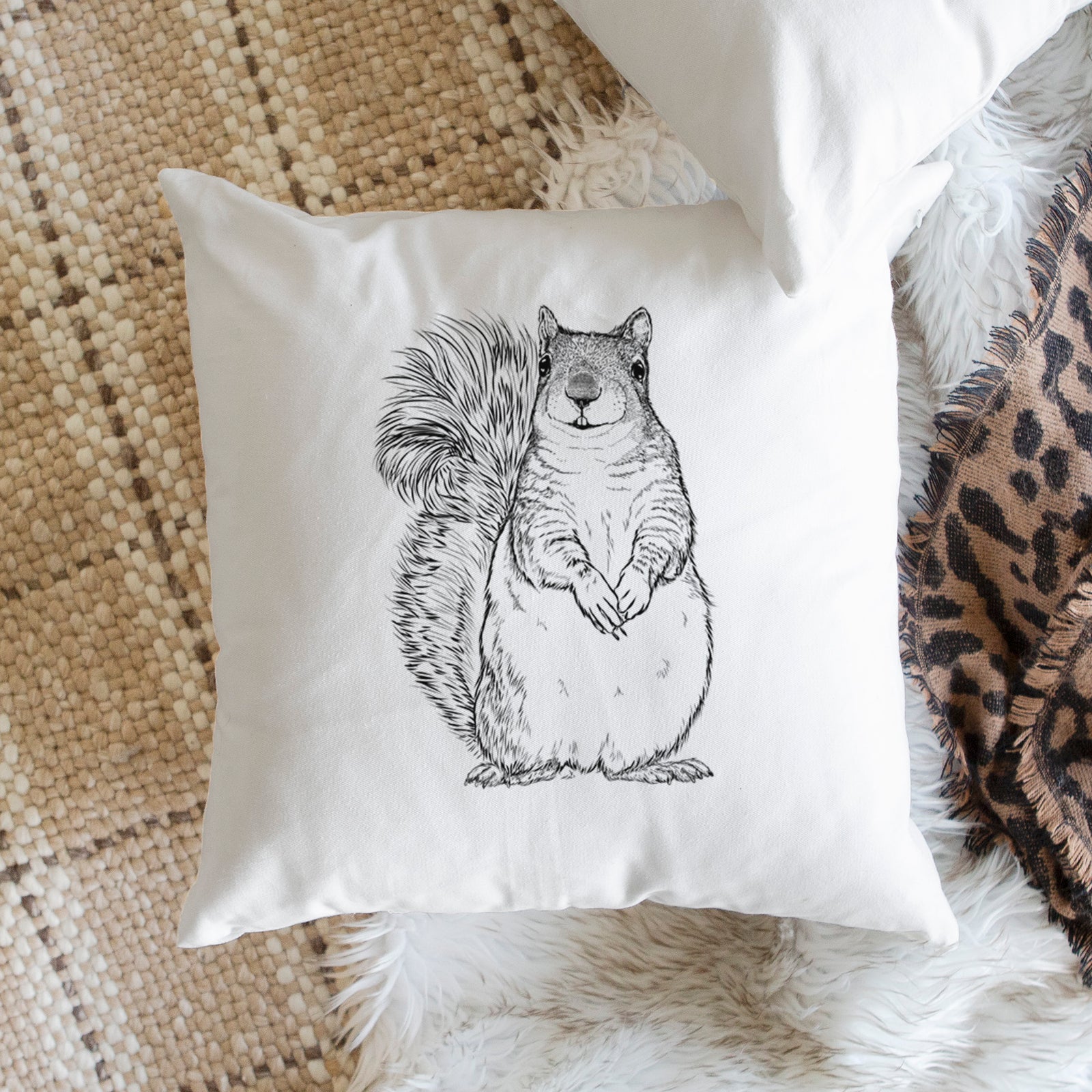 White pillow cover printed with a detailed black ink illustration of a western grey squirrel sitting upright with a bushy tail, on a bench beside plants.