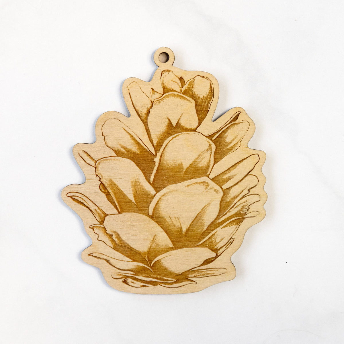 Wooden ornament featuring a detailed engraving of a western hemlock pine cone, on a marble surface.