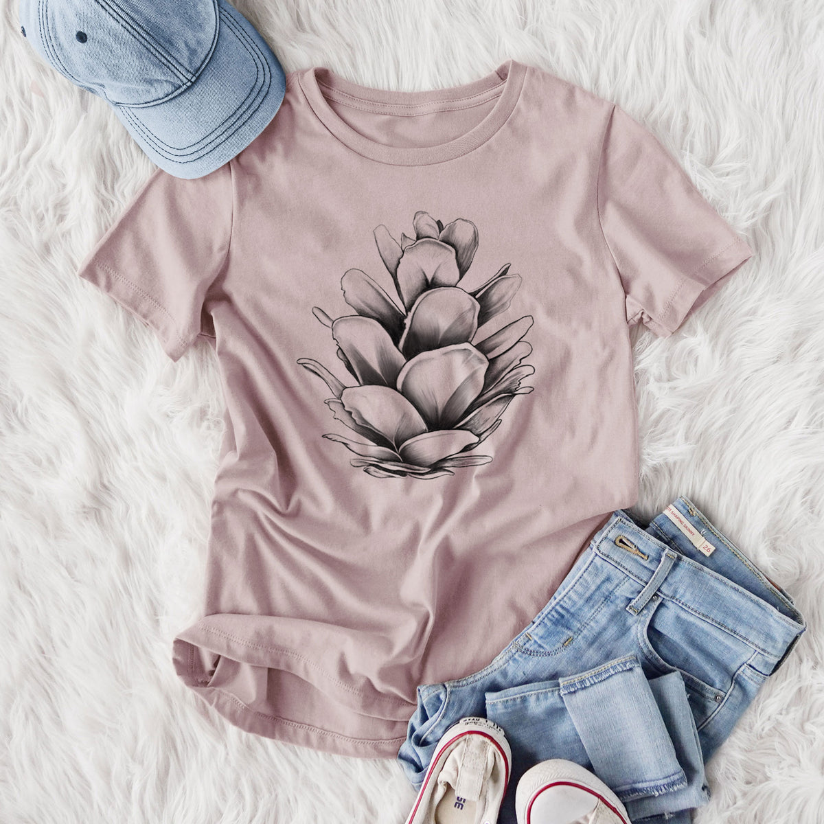 Women's relaxed fit cotton t-shirt printed with a detailed black ink illustration of a western hemlock pine cone, styled flat on a white faux fur rug with jeans.