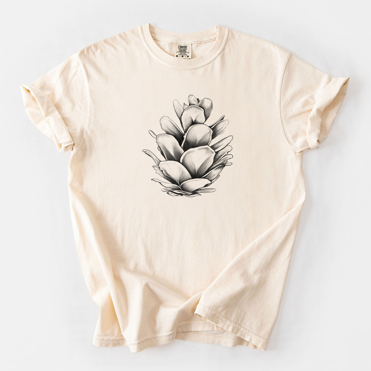 Ivory Comfort Colors t-shirt laid flat, printed with a detailed black ink illustration of a western hemlock pine cone.