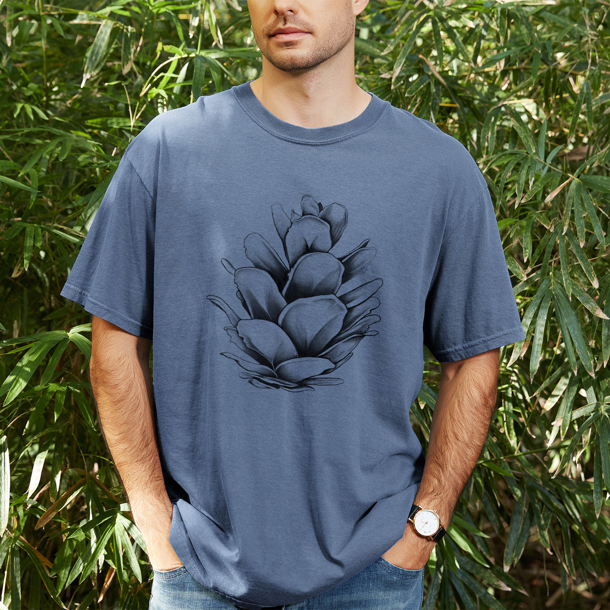 Man wearing a Comfort Colors t-shirt printed with a detailed black ink illustration of a western hemlock pine cone, outdoors.