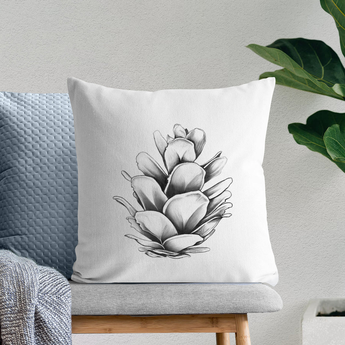 White pillow cover printed with a detailed black ink illustration of a western hemlock pine cone, on a bench beside plants.