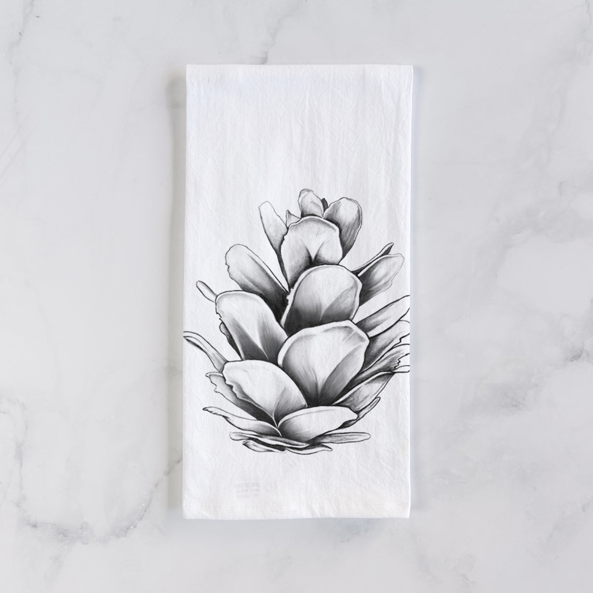 White cotton tea towel laid flat on marble, printed with a detailed black ink illustration of a western hemlock pine cone.