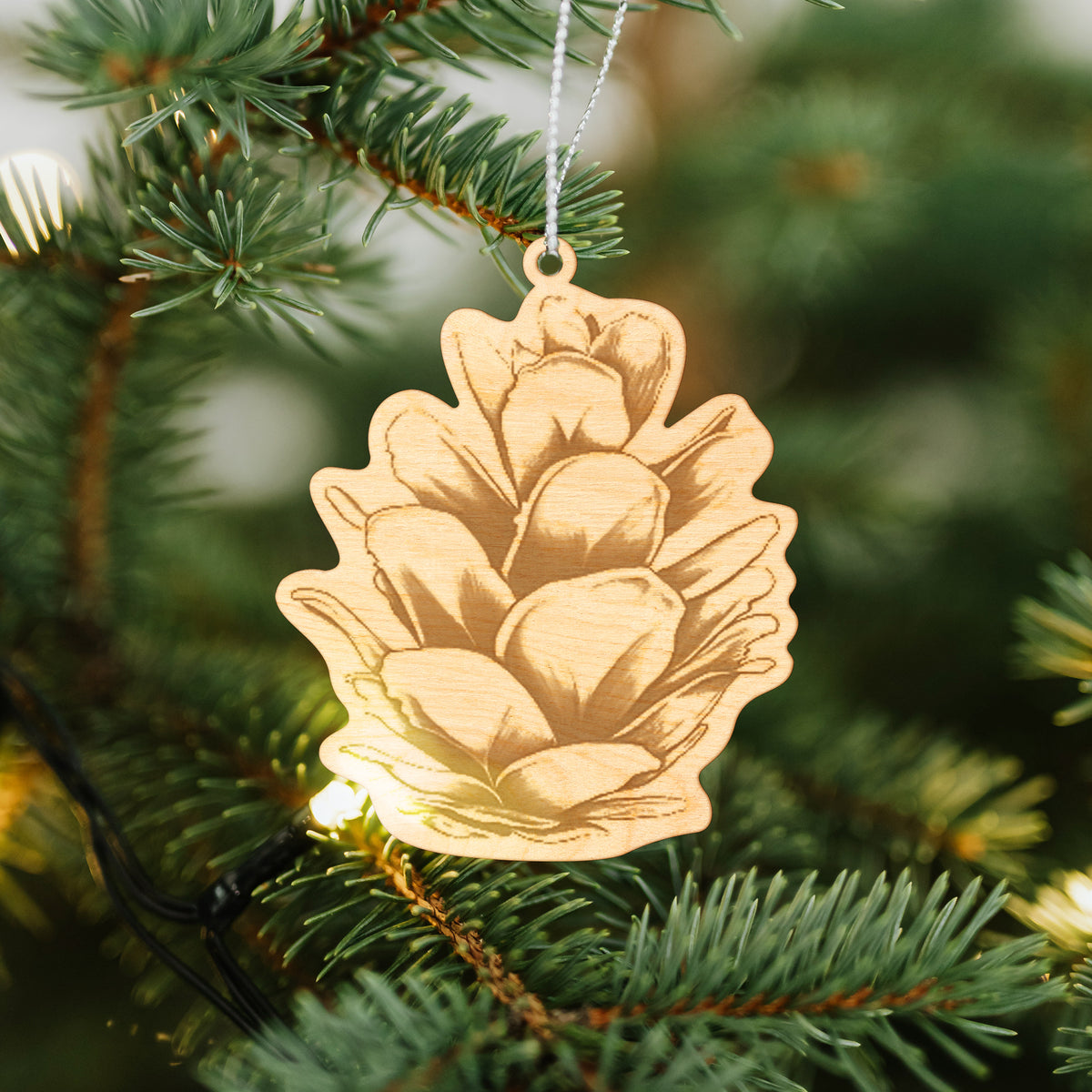 Wooden ornament featuring a detailed engraving of a western hemlock pine cone, hanging on a Christmas tree.