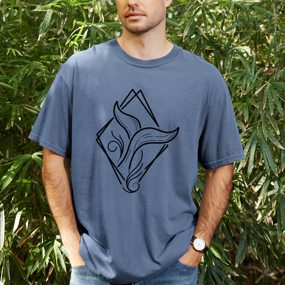 Man wearing a Comfort Colors t-shirt printed with a black line art whale tail rising from a wave inside a diamond outline, outdoors.
