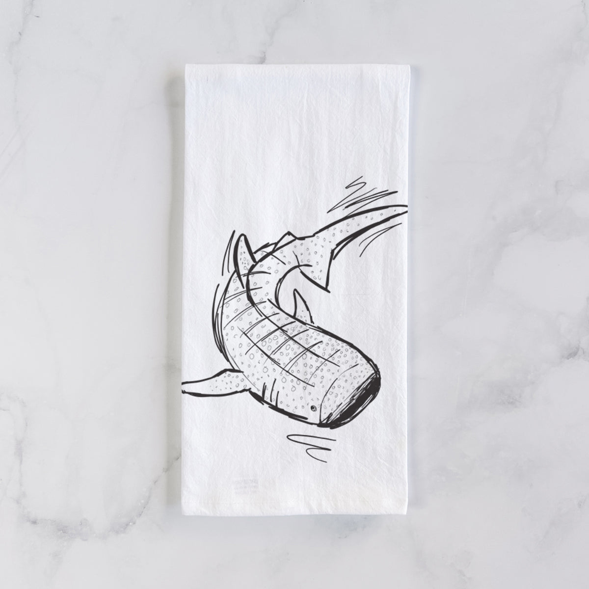 White cotton tea towel laid flat on marble, printed with a black ink illustration of a spotted whale shark swimming.
