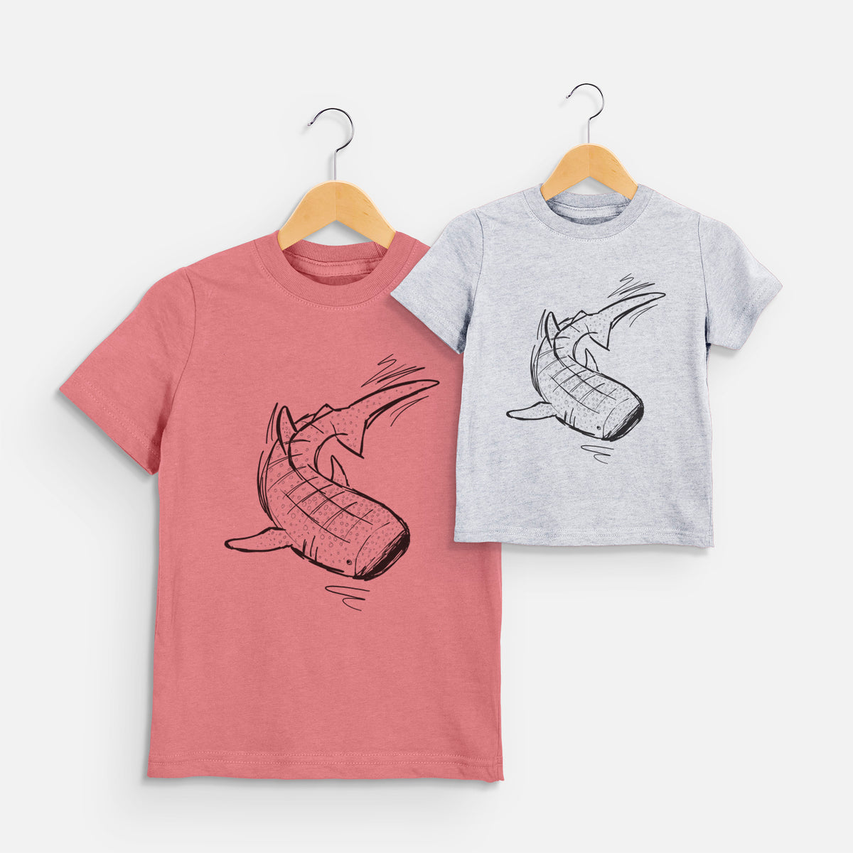 Two youth t-shirts in different colors on hangers, printed with a black ink illustration of a spotted whale shark swimming.