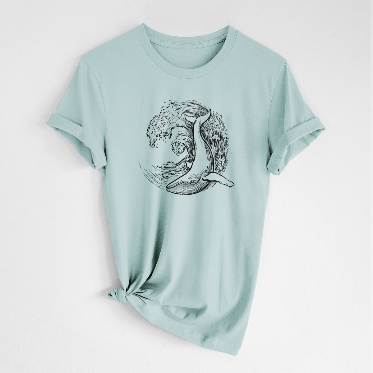 Dusty blue lightweight cotton t-shirt laid flat with the sleeves rolled, printed with a black ink illustration of a humpback whale swimming inside a curling ocean wave.