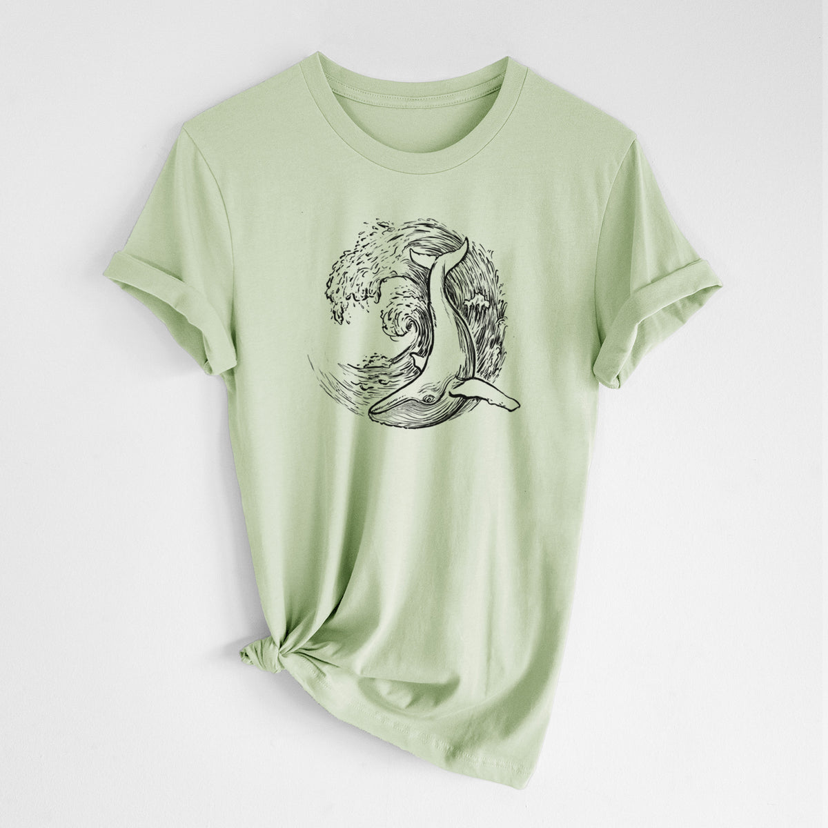 Spring green lightweight cotton t-shirt laid flat with the sleeves rolled, printed with a black ink illustration of a humpback whale swimming inside a curling ocean wave.