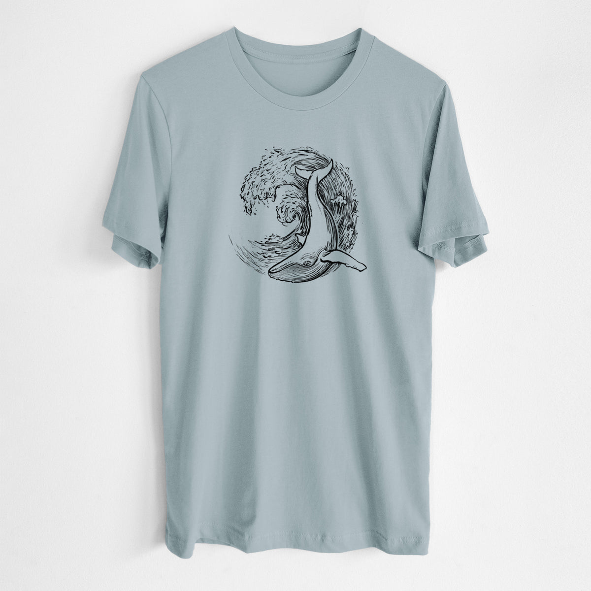 Vintage denim lightweight cotton t-shirt laid flat, printed with a black ink illustration of a humpback whale swimming inside a curling ocean wave.